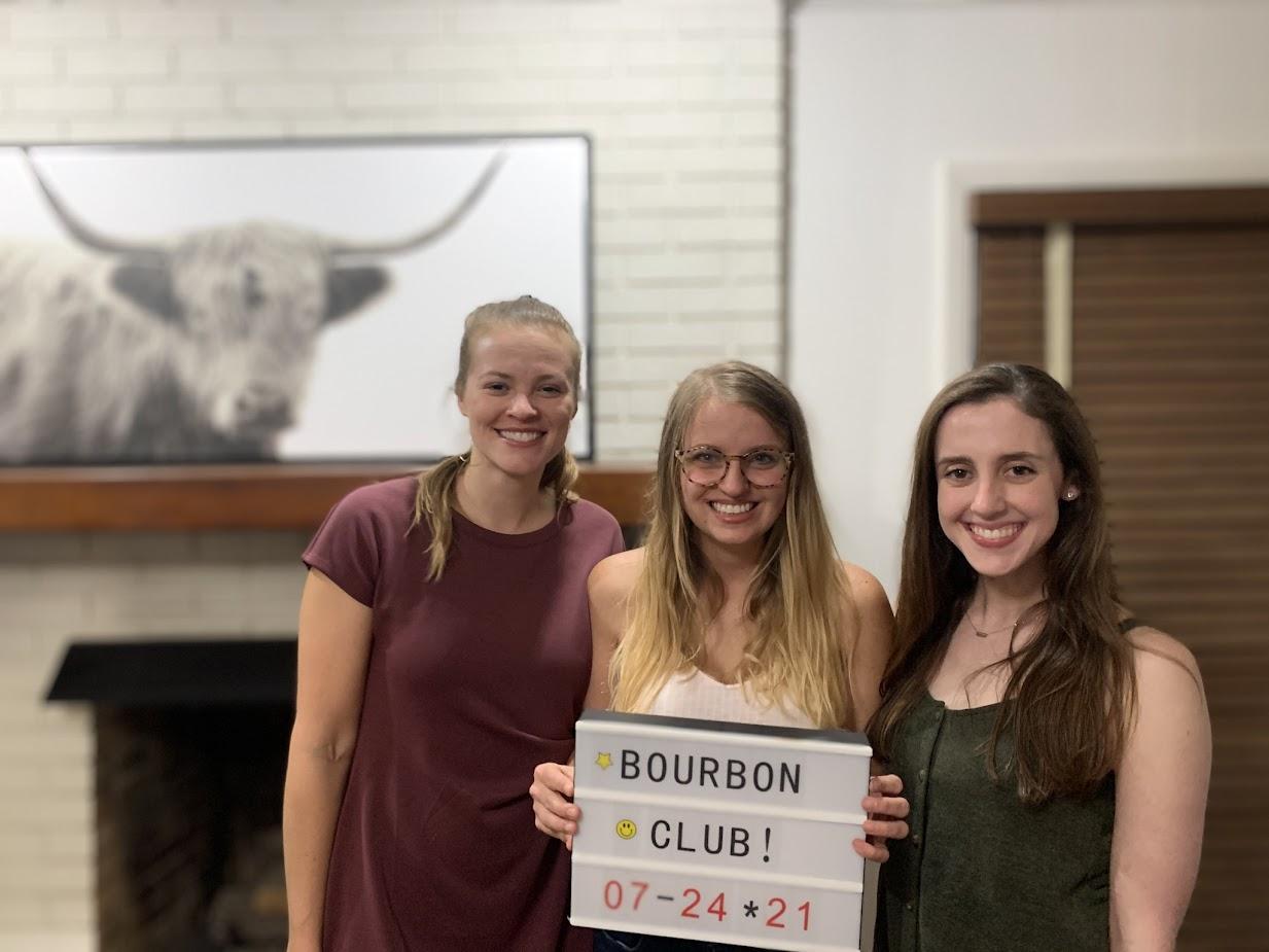 group picture of three pediatric residents with person in center holding up sign that reads Bourbon Club! July 24, 2021